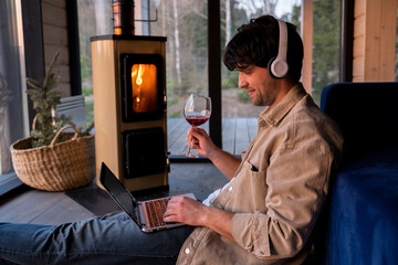 Smiling freelancer drinking wine and using a laptop in the living room sitting on the floor by the fireplace. 