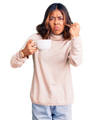 Young beautiful mixed race woman holding a cup of coffee annoyed and frustrated shouting with...