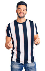 Young handsome hispanic man wearing striped tshirt very happy and excited doing winner gesture with arms raised, smiling and screaming for success. celebration concept.