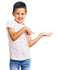 Little cute boy kid wearing casual white tshirt amazed and smiling to the camera while presenting with hand and pointing with finger.