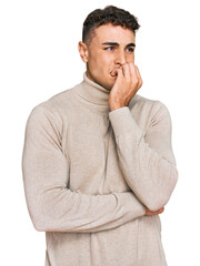 Hispanic young man wearing casual turtleneck sweater looking stressed and nervous with hands on mouth biting nails. anxiety problem.