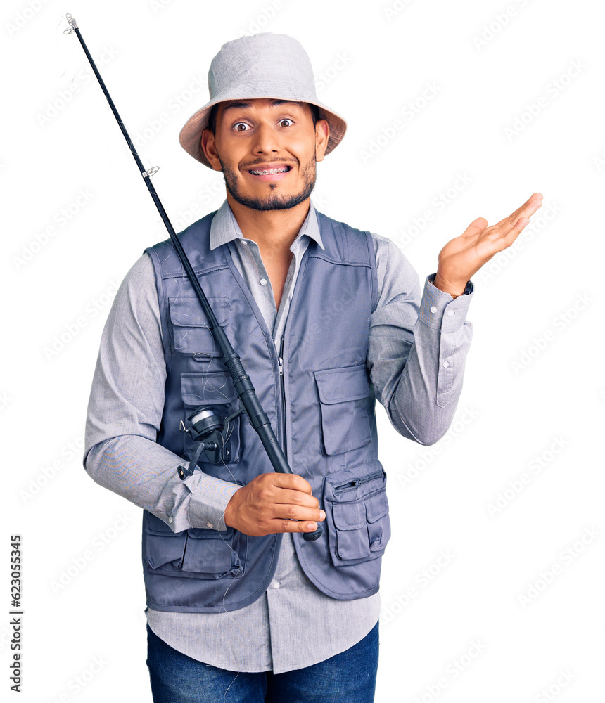 Sticker Handsome latin american young man wearing fisherman equipment celebrating victory with happy smile and winner expression with raised hands