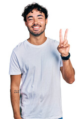 Fototapeta premium Hispanic young man with beard wearing casual white t shirt showing and pointing up with fingers number two while smiling confident and happy.