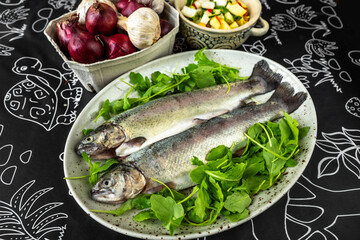 2 trout garnished with leaf, onion, garlic and salad on black.