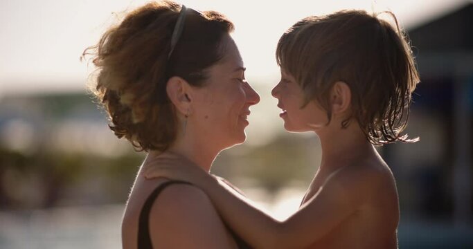 Slow motion portrait. Caucasian mom and kid smile happily and gently, lovingly rub their noses, hugging in setting sun. Concept of motherhood, tenderness, love. Loving mom and her wonderful little kid