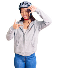 Young beautiful chinese girl wearing bike helmet smiling making frame with hands and fingers with happy face. creativity and photography concept.