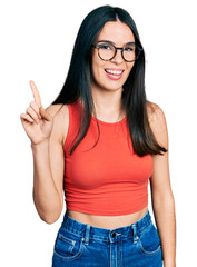 Obraz premium Young hispanic woman wearing casual clothes and glasses smiling with an idea or question pointing finger up with happy face, number one