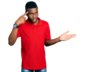 Young african american man wearing casual red t shirt confused and annoyed with open palm showing copy space and pointing finger to forehead. think about it.