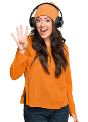 Beautiful brunette young woman listening to music using headphones showing and pointing up with fingers number four while smiling confident and happy.