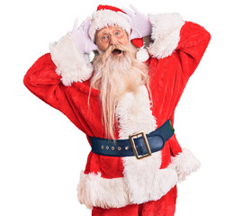Old senior man with grey hair and long beard wearing traditional santa claus costume smiling cheerful playing peek a boo with hands showing face. surprised and exited