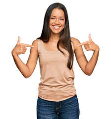 Beautiful hispanic woman wearing casual clothes looking confident with smile on face, pointing...