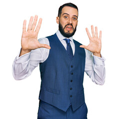Young man with beard wearing business vest afraid and terrified with fear expression stop gesture with hands, shouting in shock. panic concept.