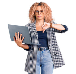 Young blonde woman with curly hair working using laptop with angry face, negative sign showing...
