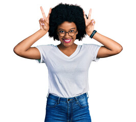Young african american woman wearing casual white t shirt posing funny and crazy with fingers on head as bunny ears, smiling cheerful