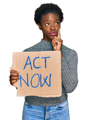 Young african american girl holding act now banner serious face thinking about question with hand...