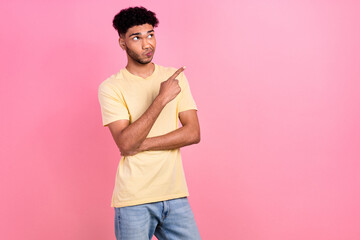 Portrait of young guy indicate finger side empty space not sure good or bad news wear shirt jeans isolated pink color background