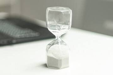 Hourglass near laptop computer concept for time management and countdown to deadline.