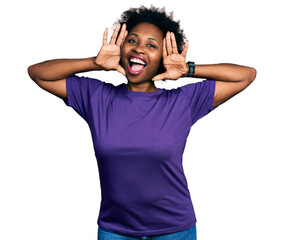 African american woman with afro hair wearing casual purple t shirt smiling cheerful playing peek a boo with hands showing face. surprised and exited