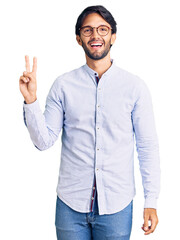 Handsome hispanic man wearing business shirt and glasses smiling looking to the camera showing fingers doing victory sign. number two.