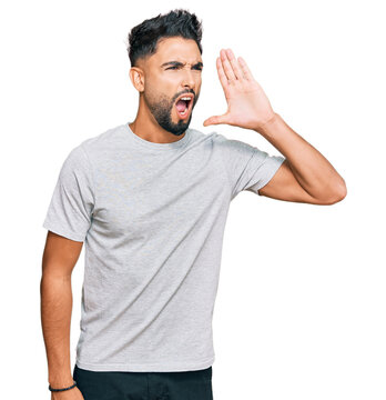 Young man with beard wearing casual grey tshirt shouting and screaming loud to side with hand on mouth. communication concept.