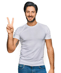 Young hispanic man wearing casual white t shirt showing and pointing up with fingers number two while smiling confident and happy.