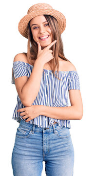 Young beautiful girl wearing hat and t shirt looking confident at the camera smiling with crossed arms and hand raised on chin. thinking positive.