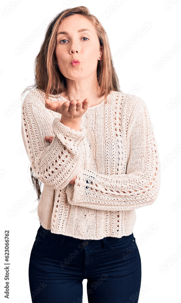 Poster young beautiful blonde woman wearing casual sweater looking at the camera blowing a kiss with hand o