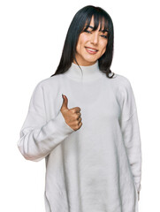 Young brunette woman with bangs wearing casual turtleneck sweater doing happy thumbs up gesture with hand. approving expression looking at the camera showing success.