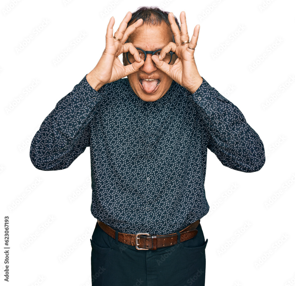 Sticker Middle age indian man wearing casual clothes and glasses doing ok gesture like binoculars sticking tongue out, eyes looking through fingers. crazy expression.