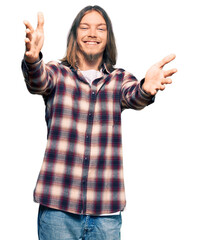 Handsome caucasian man with long hair wearing hipster shirt looking at the camera smiling with open arms for hug. cheerful expression embracing happiness.