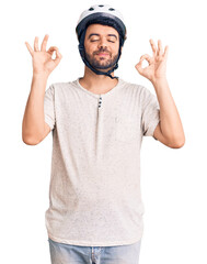 Young hispanic man wearing bike helmet relax and smiling with eyes closed doing meditation gesture with fingers. yoga concept.