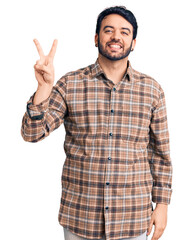 Naklejka premium Young hispanic man wearing casual clothes smiling looking to the camera showing fingers doing victory sign. number two.