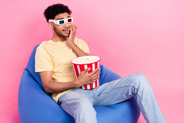 Photo of young scared guy biting nails bucket popcorn sit bean bag wear 3d goggles thriller horror movie isolated on pink color background