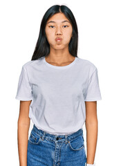 Obraz premium Beautiful young asian woman wearing casual white t shirt puffing cheeks with funny face. mouth inflated with air, crazy expression.