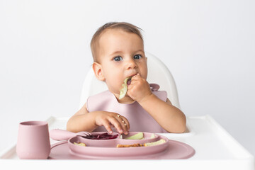 little cute girl eats complementary foods in a highchair, close up portrait on white background