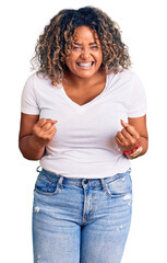 Young african american plus size woman wearing casual clothes very happy and excited doing winner gesture with arms raised, smiling and screaming for success. celebration concept.