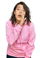 Young hispanic woman wearing casual sweatshirt hand on mouth telling secret rumor, whispering malicious talk conversation