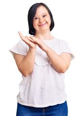 Brunette woman with down syndrome wearing casual white tshirt clapping and applauding happy and...