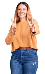 Beautiful young woman wearing casual clothes smiling looking to the camera showing fingers doing victory sign. number two.