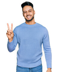 Fototapeta premium Young arab man wearing casual clothes smiling with happy face winking at the camera doing victory sign. number two.