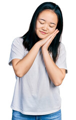 Young chinese woman wearing casual white t shirt sleeping tired dreaming and posing with hands together while smiling with closed eyes.