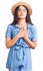 Brunette teenager girl wearing summer hat smiling with hands on chest with closed eyes and grateful gesture on face. health concept.