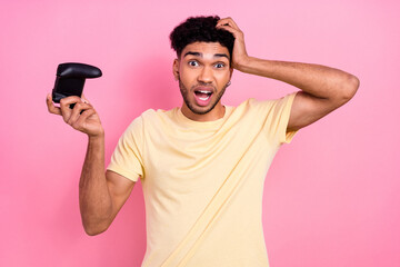 Portrait of astonished disappointed man dressed yellow t-shirt hold joystick arm on head lose game...
