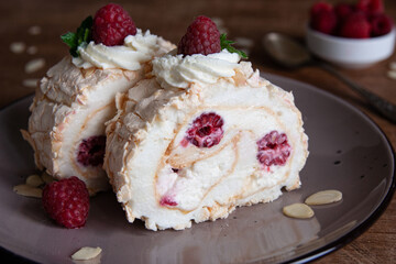 Two bites of meringue roll with cream, raspberries and almond petals. Dark wooden background. Close-up.