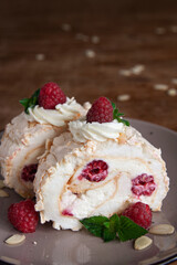 Two bites of meringue roll with cream, raspberries and almond petals. Dark wooden background. Close-up. Vertical