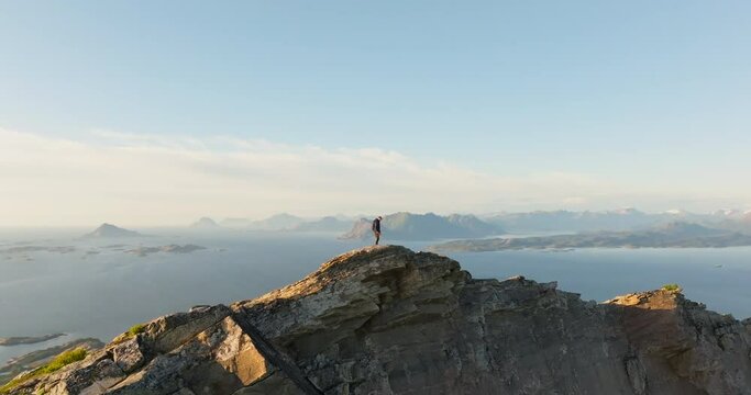Norway hiker on mountain with panorama island view in midnight sun sunset; drone
