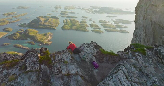 Female on Norway mountain vertical cliff edge admire panorama midnight sun