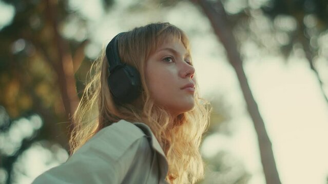 Beautiful woman listens to podcast in nature, backlit by sunset, side view 