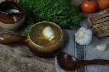 hot fresh soup in plate on rustic wooden table, vegetables are laid out around, red tomatoes, bread, garlic, dill greens, old utensils, concept of cooking homemade traditional food, healthy eating