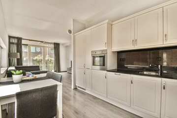 a kitchen with white cabinets and black counter tops in the center of the photo is taken from the living room to the dining area